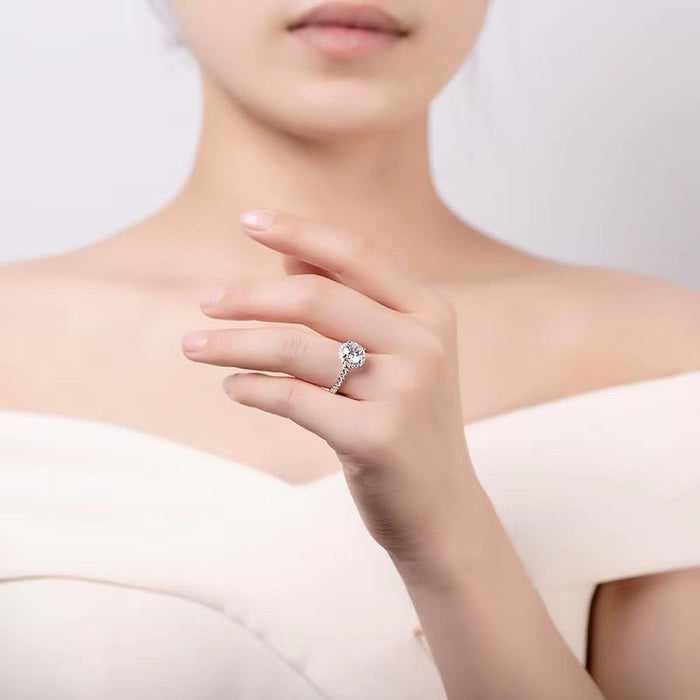 白いドレスの胸元でモアサナイトの婚約指輪を着けた女性の手元