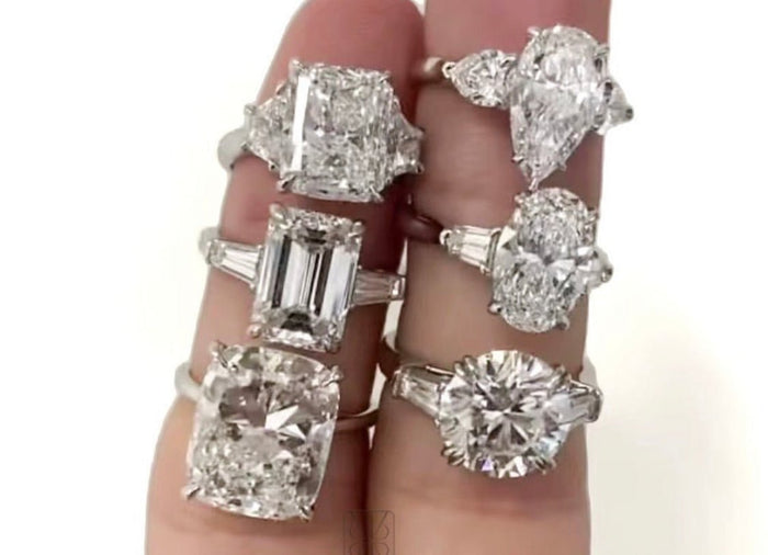 指の間に並べた大粒のエメラルドカットやペアシェイプの婚約指輪6本