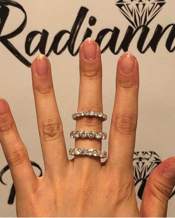 Radiannのロゴを背に3本のフルエタニティリングを重ね着けした手