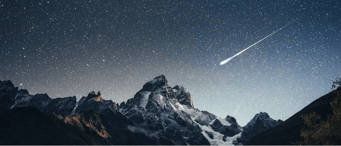 流れ星が横切る星空と雪をかぶった山の稜線