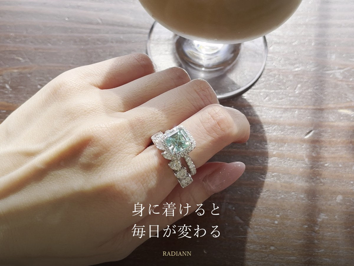 アイスカフェオレの横でグリーンの石のリングとエタニティリングを重ね着けした手元