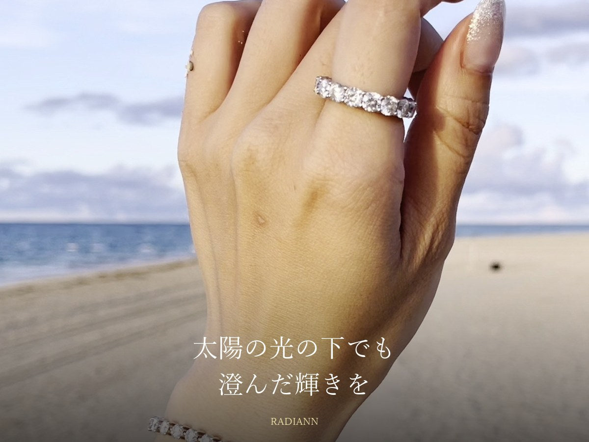 海辺の太陽の光の下でモアサナイトのリングとテニスブレスレットを着けた手元